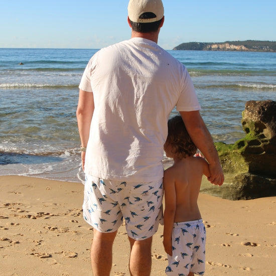Man and child holding hands on a beach in matching boardies